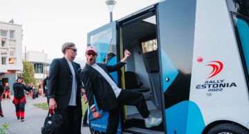 Two men preparing to board an Auve Tech autonomous shuttle with WRC Rally Estonia branding.