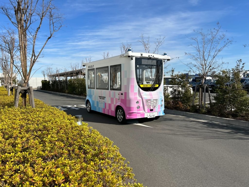 Auve Tech autonomous shuttle operated by Boldly driving on a tree-lined road under a clear blue sky