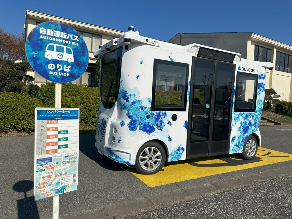 Auve Tech autonomous shuttle at a bus stop in Japan with a blue bus stop sign in the foreground