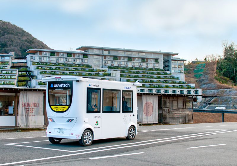 Auve Tech autonomous shuttle driving in front of a building and coffee shop in Japan