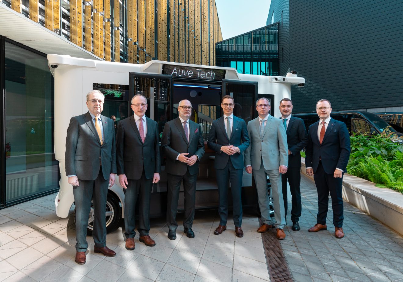 Alexander Stubb, Väino Kaldoja, and a group of executives posing in front of an Auve Tech autonomous shuttle.