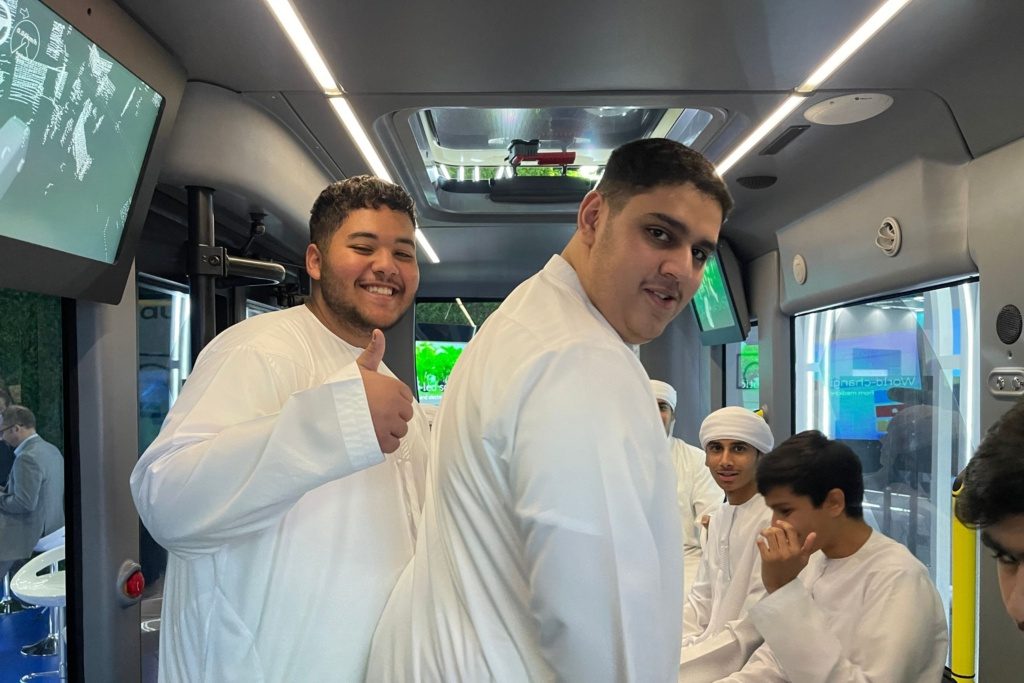 Group of young men in traditional attire inside the Auve Tech MiCa autonomous shuttle at ITS World Congress 2024 event.